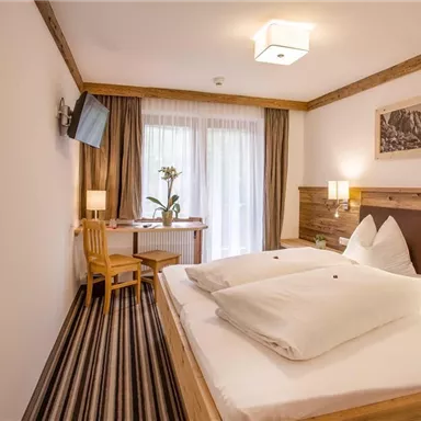 Ein gemütliches Hotelzimmer mit zwei Betten, einem Tisch und Stühlen. Große Fenster lassen viel Licht herein und bieten einen Blick auf die Natur.