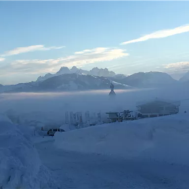 A snow-covered landscape with mountains in the background and a misty sky. The shoreline is covered in snow and it is very quiet.