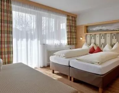 A cozy room with two beds and a seating area. Large windows provide plenty of daylight.