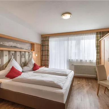 A cozy room with a double bed and red cushions. Large windows provide plenty of daylight and a pleasant atmosphere.