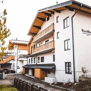 Ein modernes, mehrstöckiges Gebäude mit Holzverkleidungen in einer ländlichen Umgebung. Der Garten ist gepflegt und von Bäumen umgeben.