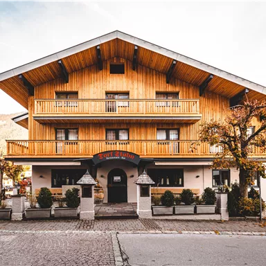 Ein traditionelles Holzhaus mit mehreren Balkonen und einem großzügigen Eingangsbereich. Die Fassade hat einen warmen, einladenden Charakter und ist von kleinen Bäumen umgeben.