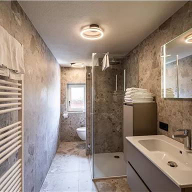 A modern bathroom with an elegant shower and a stylish sink. The walls are designed in a warm gray tone, and there is a metallic towel holder.