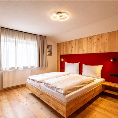 A modern bedroom with a wooden bed and white pillows. Large windows provide plenty of daylight.