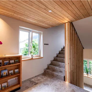 A beautiful hallway with a wooden ceiling and staircase. The windows let in a lot of light and plants create a pleasant atmosphere.