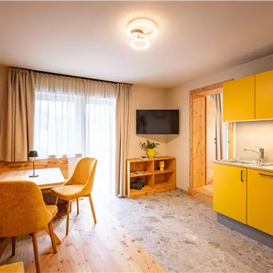 A modern apartment with a bright yellow kitchen and a dining table. Large windows provide plenty of daylight and a cozy atmosphere.