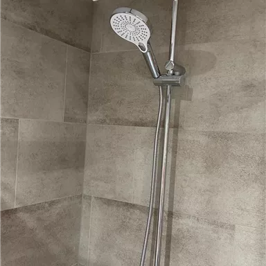 A modern shower with a large rain shower and a hand shower. The walls are clad with brown tiles.