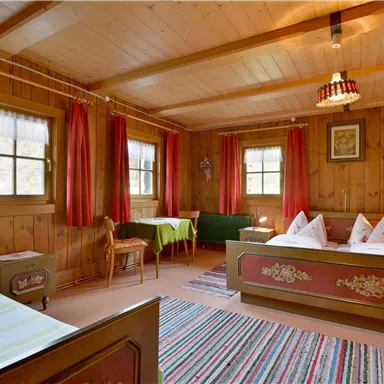 A cozy room with wooden paneling and red curtains. There are two beds, a table, and a carpet.