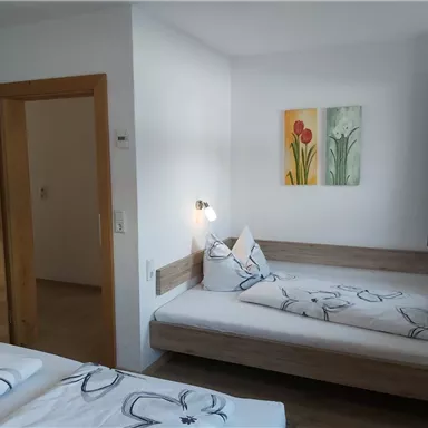 A bright room with two beds and flower decorations. Colorful pictures hang on the wall, and a window lets in plenty of light.