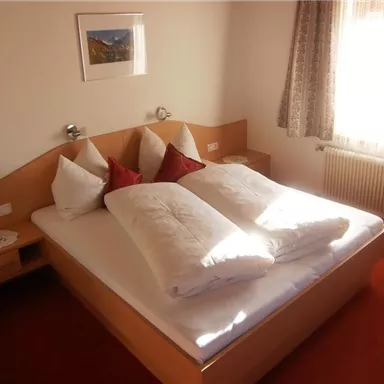 A cozy bedroom with a large double bed and two pillows. The room is bright and cheerful, with a window that lets in sunlight.