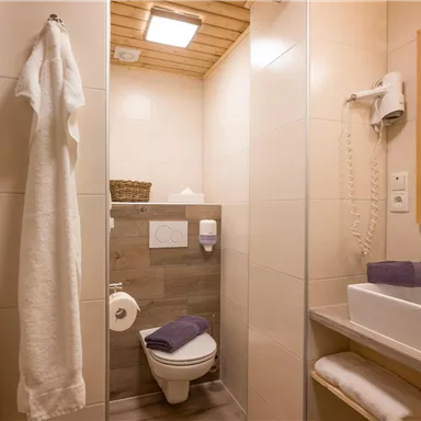 A modern bathroom with bright tiles and wooden details. There is a sink, a toilet, and towels in soft colors.