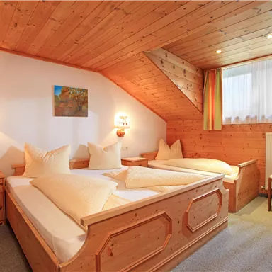 A cozy room with wooden paneling and two beds. At the window, there is a view of daylight and a small art canvas on the wall.