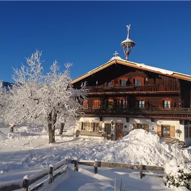A traditional wooden house in a snowy landscape. Surrounded by snow-covered trees and clear blue sky.