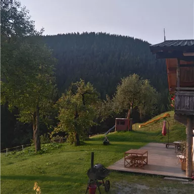 Ein schöner Garten mit einer Holzhütte und einer Berglandschaft im Hintergrund. Ein Heißluftballon schwebt am Himmel.