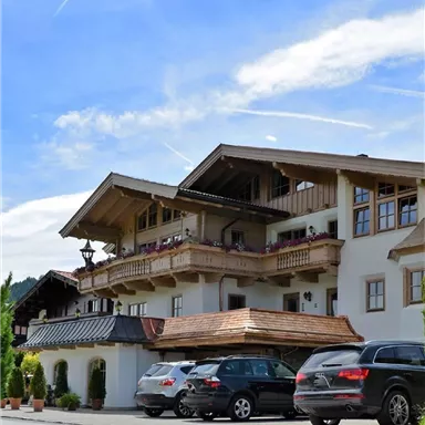 A beautiful alpine building with traditional architecture and a spacious balcony. Several cars are parked in front of the building.