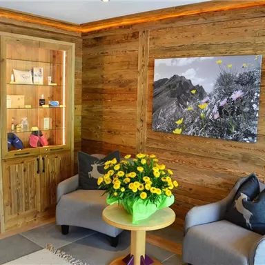 An inviting room with wooden-paneled walls, two cozy armchairs, and a round table. On the table is a bouquet of flowers, and on the wall hangs a black-and-white picture with colorful flowers.