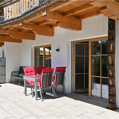 Eine gemütliche Terrasse mit rotem Mobiliar und einem Tisch. Der Bereich ist umgeben von modernen Holzstrukturen und bietet Zugang zu Fenstern.