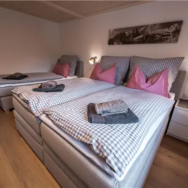 A cozy bedroom with three beds and checked bedspreads. The walls are brightly painted and there are modern bedside lamps.