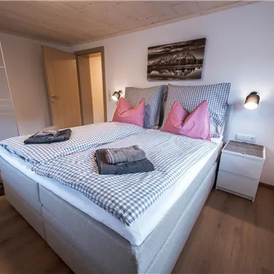A stylish bedroom with a large bed and pink pillows. The room has a modern look with hardwood flooring and simple furniture.