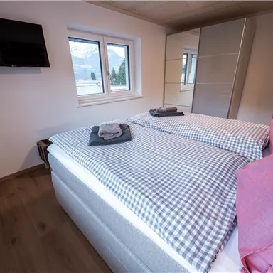 A modern bedroom with two single beds and striped bedcovers. Windows let in plenty of daylight, and there is a television on the wall.