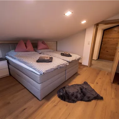 A cozy bedroom with two beds and pillows. The room has a wooden floor and an open door that leads to another area.