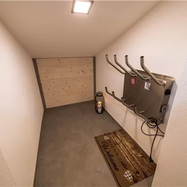 A small, bright room with a gray floor and a wooden wall. Several brackets are hanging on the wall and there is an electric heater on the floor.