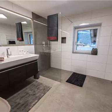 A modern bathroom with a glass shower and a wide sink unit. Bright tiles and dark furniture create an elegant look.
