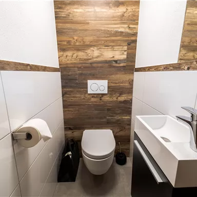 A modern bathroom with wooden paneling and elegant sanitary facilities. It includes a toilet, a sink, and a toilet paper holder.