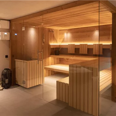 A modern sauna room with wooden elements and gentle lighting. The glass front creates a bright and inviting atmosphere.