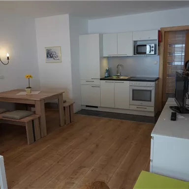 Ein modernes Wohnzimmer mit einer offenen Küche. Es gibt einen Esstisch, eine Couch und einen Fernseher.
