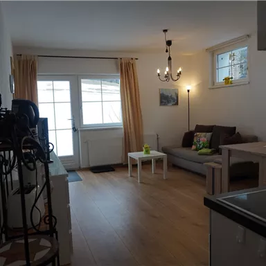 Ein helles Wohnzimmer mit einer gemütlichen Couch und einem kleinen Tisch. Große Fenster lassen viel Licht herein und schaffen eine einladende Atmosphäre.