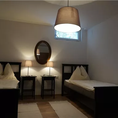 Ein helles Schlafzimmer mit zwei Einzelbetten und einem runden Spiegel. Neben den Betten stehen zwei Nachttische mit Lampen.
