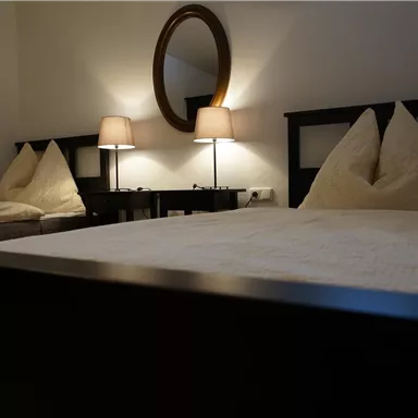 Ein gemütliches Schlafzimmer mit zwei Betten und warmem Licht. Die Wände sind in neutralen Farben gehalten, und ein runder Spiegel reflektiert die sanfte Beleuchtung.