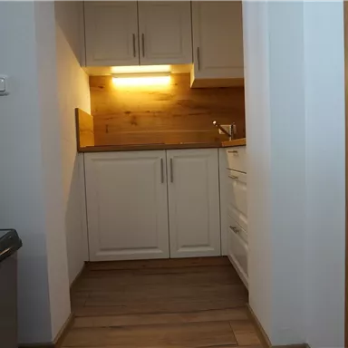 Eine moderne Küche mit weißen Schränken und Holzdetails. Der Boden ist aus Holz und es ist gut beleuchtet.