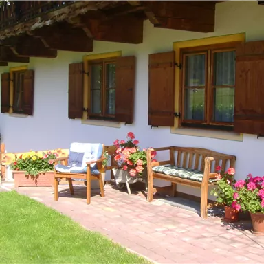 A cozy terrace in front of a bright house.
Colorful flowers and wooden benches invite you to relax.