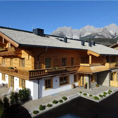 A beautiful wooden house in a picturesque mountain landscape. The surroundings are green with well-kept plants and a view of the mountains in the background.