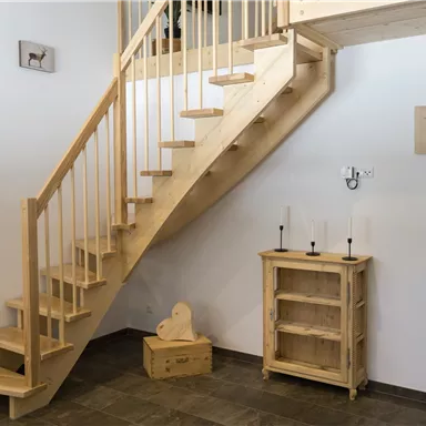 A bright entrance area with a wooden staircase and a wooden cupboard. The walls are simple and lightly designed.