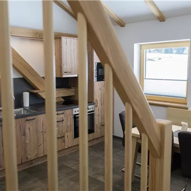 A modern kitchen with wooden cabinets and modern appliances. The room has large windows that let in a lot of daylight.