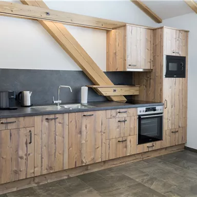 A modern wooden kitchen with stylish cabinets and a dark countertop. The equipment includes a refrigerator, an oven, and a sink.