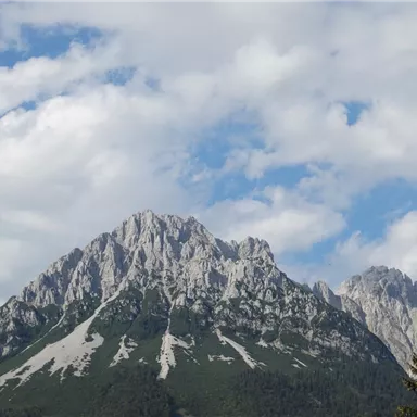 Ein atemberaubender Berg mit schroffen Felsen und grünen Hängen. Der Himmel ist teilweise bewölkt und vermittelt eine majestätische Atmosphäre.