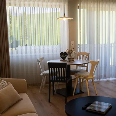 A cozy living space with a table and chairs. Large windows let in plenty of daylight.