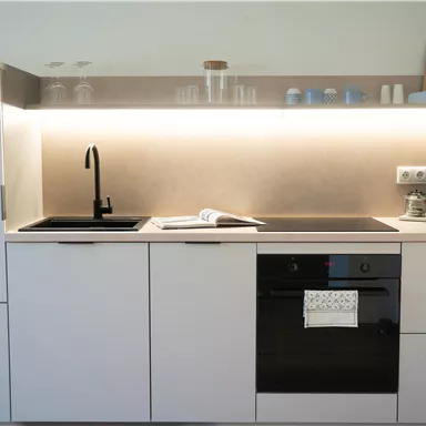 A modern kitchen with bright cabinets and elegant appliances. Under the lighting, a sink, a stove, and a coffee machine are visible.