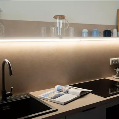 A modern kitchen with a black faucet, a cooktop, and a cooking magazine on the countertop. In the background, glasses and kitchen utensils are visible.