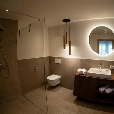 A modern bathroom with a shower, a sink, and stylish lighting. The walls and floor are in neutral shades.