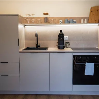 Eine moderne Küche mit minimalistischen Möbeln und einer eleganten Arbeitsfläche. Sie ist mit einem Wasserhahn, einem Kaffeeautomat und einem Herd ausgestattet.