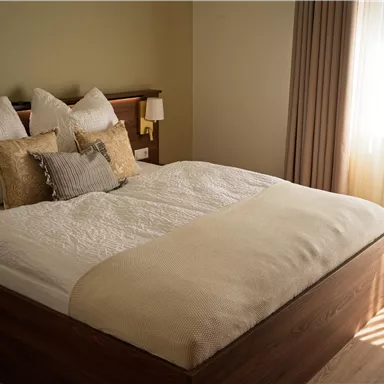 Ein modernes Schlafzimmer mit einem großen Bett und gemütlichen Kissen. Licht strömt durch das Fenster und schafft eine warme Atmosphäre.