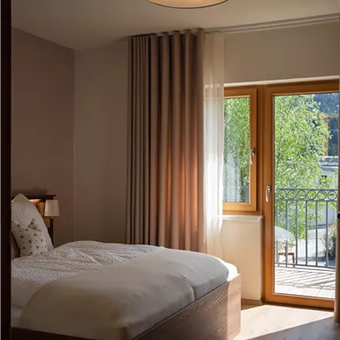 Ein gemütliches Schlafzimmer mit einem Doppelbett. Das Zimmer hat große Fenster, die viel Licht hereinlassen und einen Blick auf den Balkon bieten.
