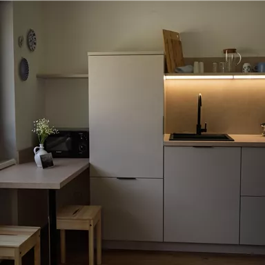 Eine moderne Küche mit minimalistischen Möbeln und einem kleinen Tisch. Das Licht beleuchtet die Arbeitsfläche und schafft eine einladende Atmosphäre.