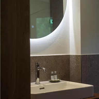 Ein modernes Badezimmer mit einem eleganten Waschbecken und einem runden Spiegel. Auf der Ablage sind zwei Fläschchen platziert.