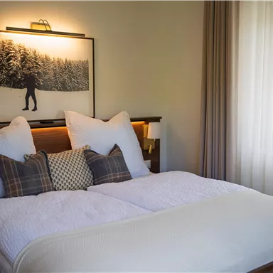 Ein gemütliches Schlafzimmer mit einem großen Bett und mehreren Kissen. Im Hintergrund hängt ein Bild eines Schneewalds.